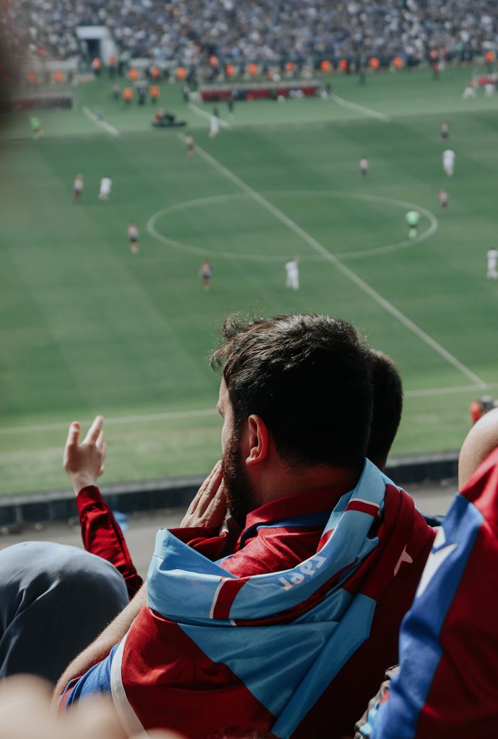Enthusiastic fan in sports jersey enjoys live football match in stadium.