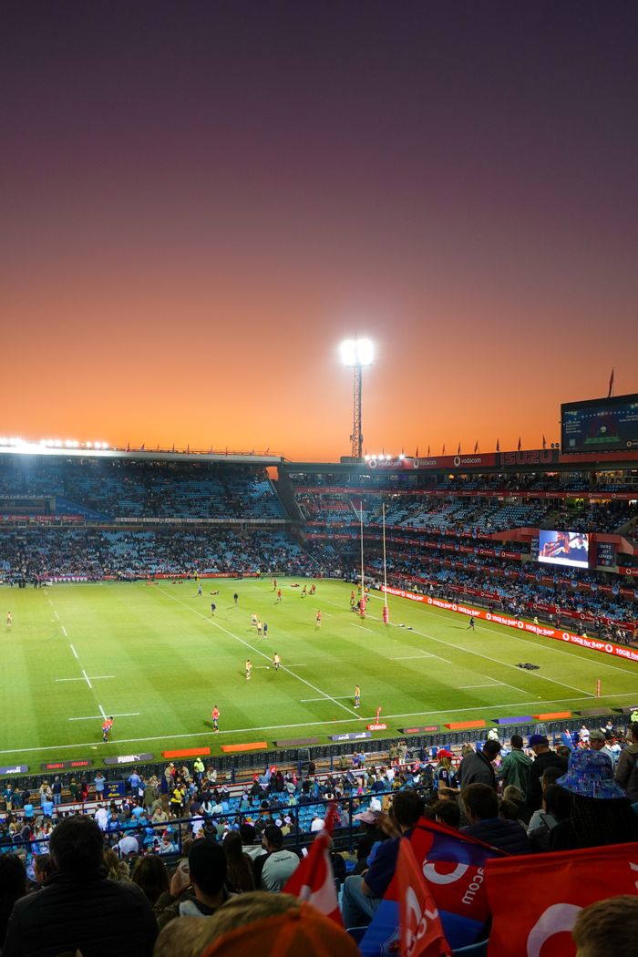 A vibrant rugby match taking place in a large stadium during sunset, with cheering crowd.